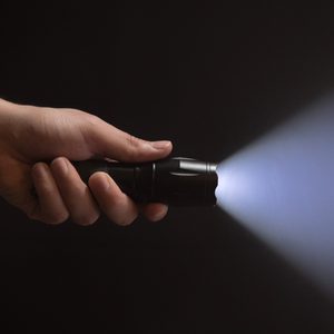 Black flashlight with wide beam in male's hand isolated from left side of the frame on black background