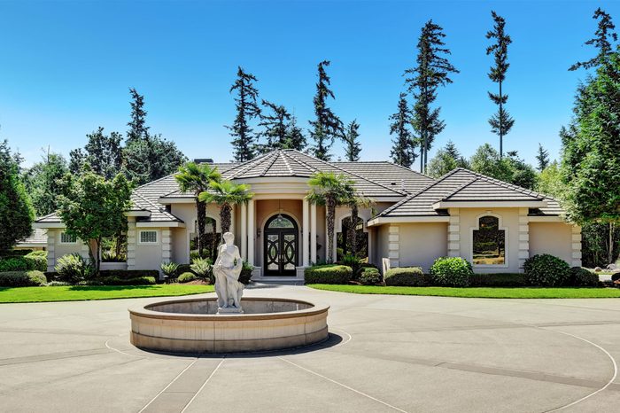 Suburban family house with fountain statue in the front yard, asphalt driveway. Luxury residential house with large windows, trees around and blue sky background. Northwest, USA