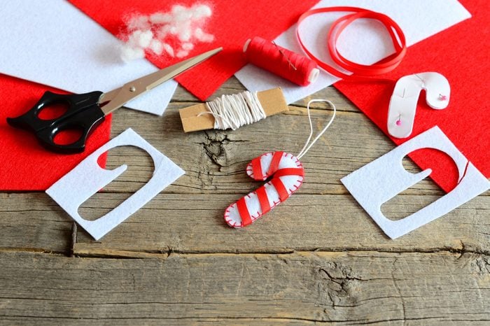 Christmas candy cane ornament felt, scissors, paper template, thread, needle, pieces and scraps of red and white felt, filler, ribbon on old wooden background.  Christmas DIY concept.  Holiday crafts for children