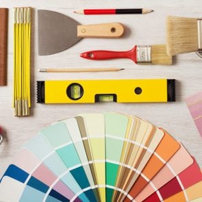 Decorator holding a painting roller and painting a wooden surface, work tools and swatches at bottom, banner with copy space
