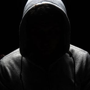 A man who's wearing a hoodie and who's face is concealed by darkness.