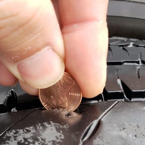 Fingers holding penny measuring tire tread depth