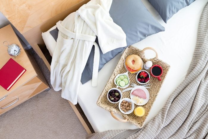 High Angle View of Bathrobe and Breakfast Tray on Unmade Bed Beside Night Table with Red Book in Hotel Room
