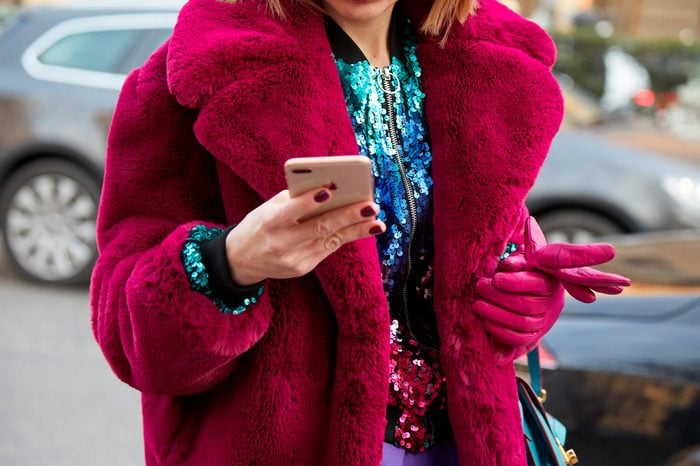 MILAN - FEBRUARY 21: Woman with pink fur coat and sequin jacket looking at smartphone before Alberta Ferretti fashion show, Milan Fashion Week street style on February 21, 2018 in Milan.