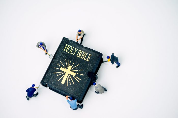 Miniature people : Worker try to fix and open Holy bible on white background