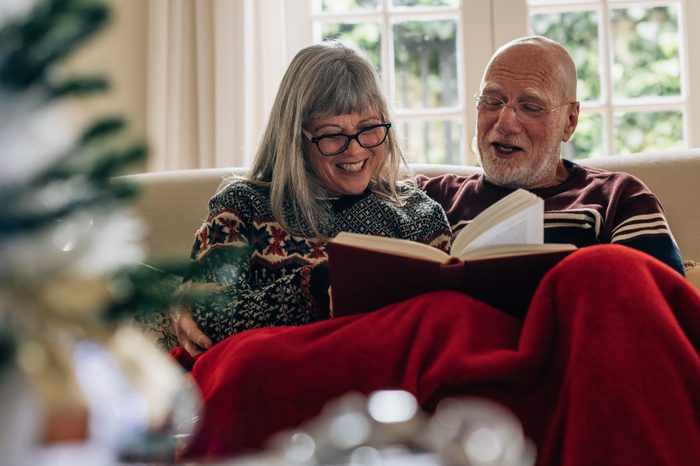 Happy senior man and woman reading a book and smiling. Old couple spending time together reading a book sitting on couch at home.