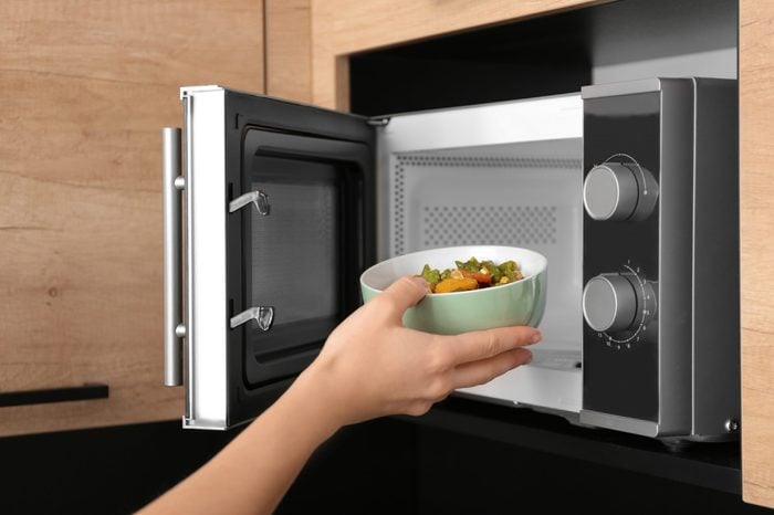 Young woman using microwave oven in kitchen