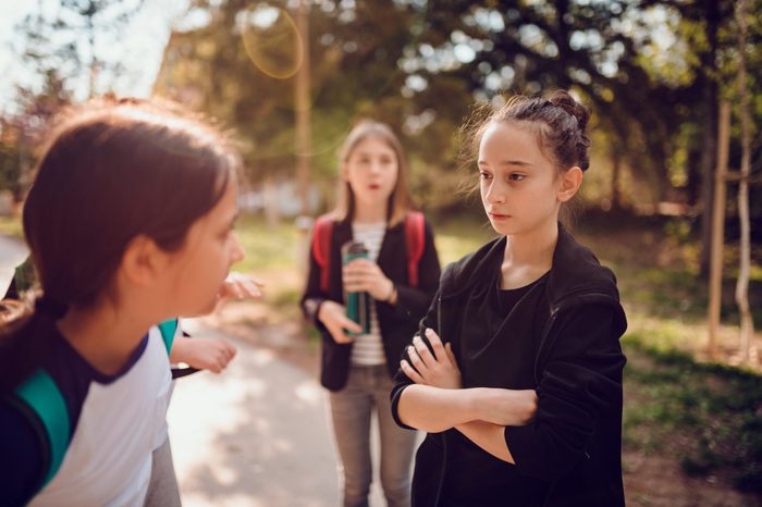 Girl wearing black hoodie bullying girl at schoolyard