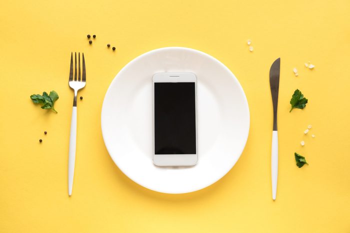 Smartphone on white plate with fork and knife. Food delivery concept on yellow background, top view, copy space.