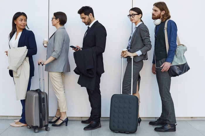Group of serious boring young multi-ethnic people with bags and luggage standing in line while passing through airport security check