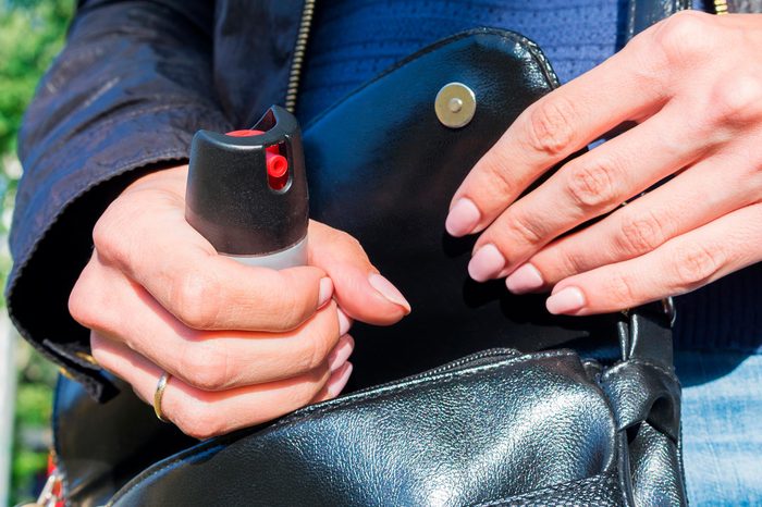 A young woman pulls a can of tear gas or bottle of pepper spray out of her purse. Means of self-defense. Selective focus, close-up.