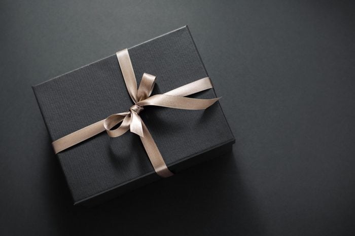 One gift wrapped in dark black paper with luxury bow on dark background. Horizontal with copy space. 