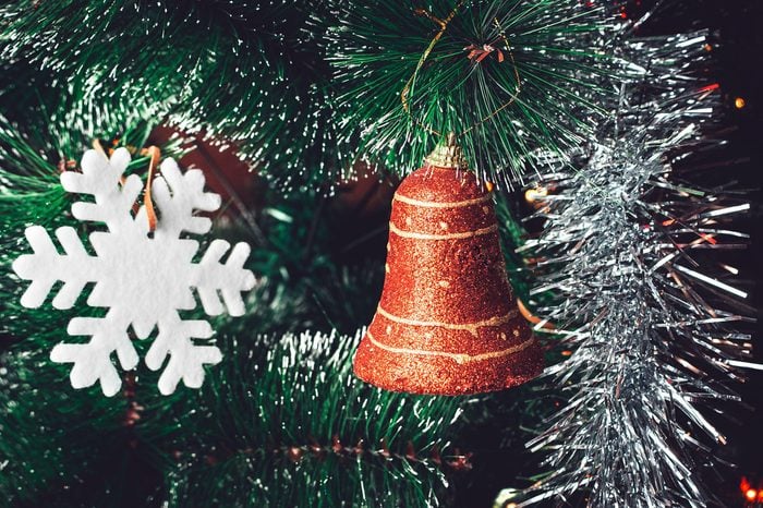 Christmas Tree Decorations: Red Orange Bell, White Snowflake, Shining Silver Tinsel on Green Needles with White Tips. Happy New Year and Christmas Concept.