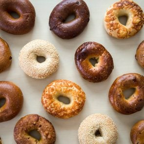 Selection of various flavors of fresh bagels on a neutral wood table background