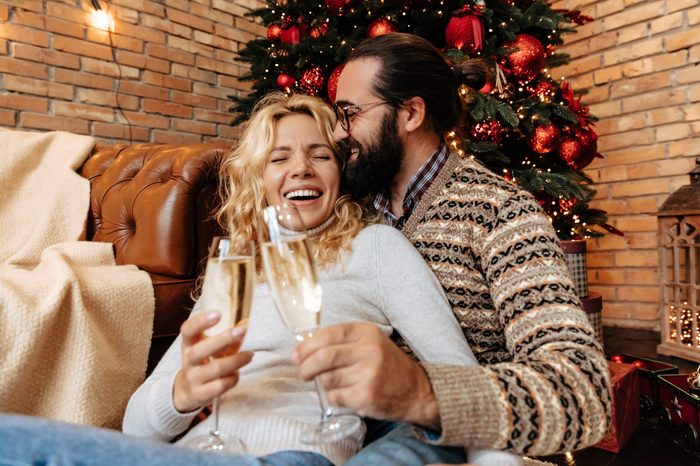 Christmas. Couple. Home. Togetherness. Man and woman are drinking champagne, hugging and laughing near the Christmas tree