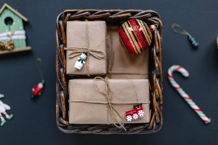 Close up flat lay photo of Christmas presents and fir toys in wooden basket. Gift boxes wrapped in kraft paper, red ball. Holiday mood. Happy New Year decoration. Merry Christmas concept. 