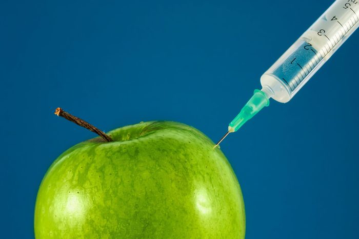 Toxin injection in Green apple by syringe. Genetically modified food (GMO). Botox injection. Aesthetic medicine. Medical background concept.