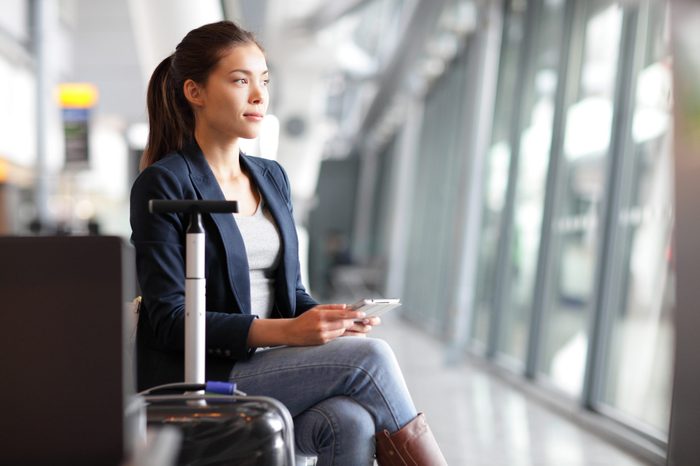 Passenger traveler woman in airport waiting for air travel using tablet smart phone. Young business woman smiling sitting with travel suitcase trolley, in waiting hall of departure lounge in airport.