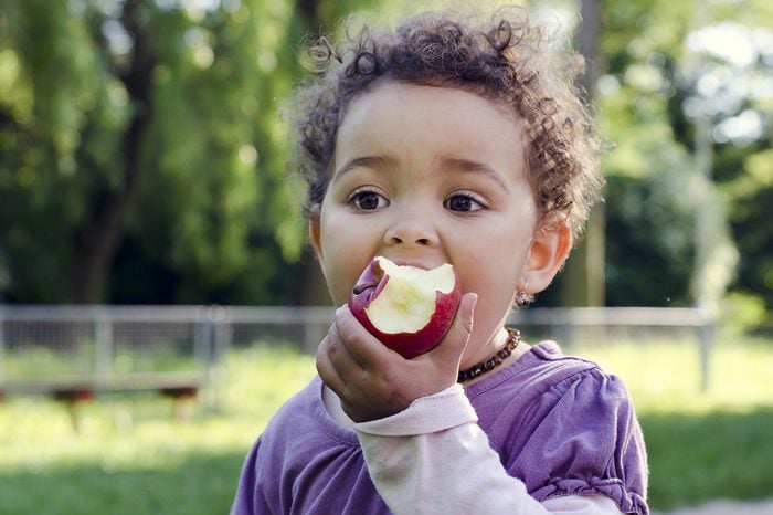 Child girl eating an apple in a park in nature.