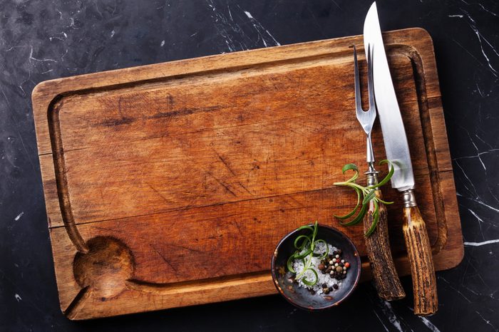 Chopping cutting board, seasonings and rosemary with fork and knife carving set on dark marble background