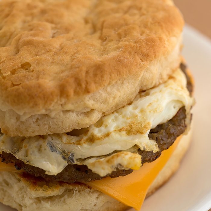 Close view of a sausage egg and cheese biscuit breakfast sandwich on a white plate upon a tan table cloth