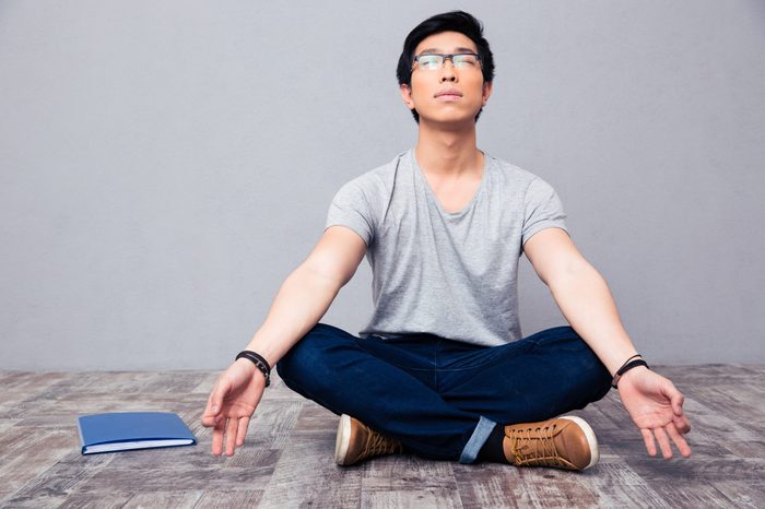 Young asian man sitting on the floor and meditating 