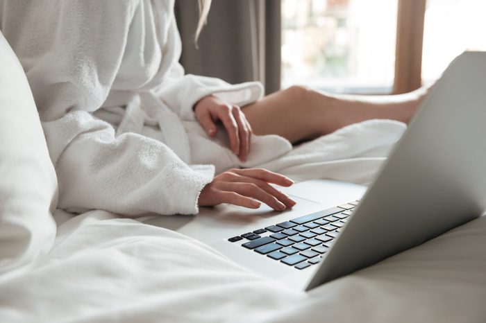 Cropped image of a woman in bathrobe on bed and using laptop in a hotel room