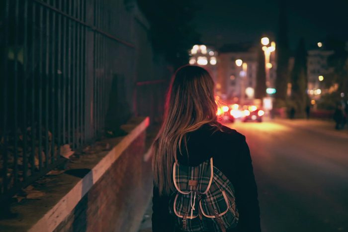 Back view of brunette woman walking near the road at the traffic time. Girl goes through the city late at night alone.
