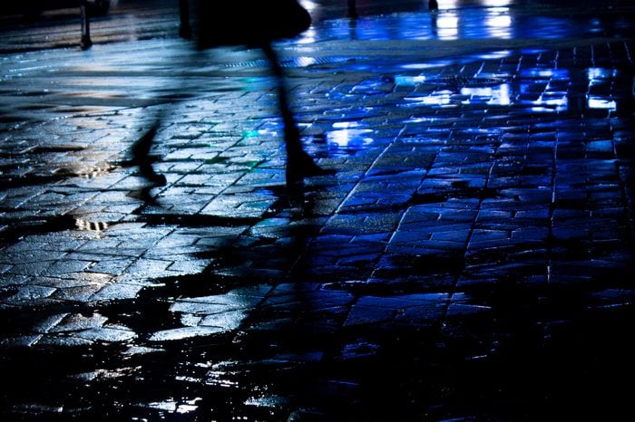 Rainy city street reflections: Legs of a young woman walking in the night