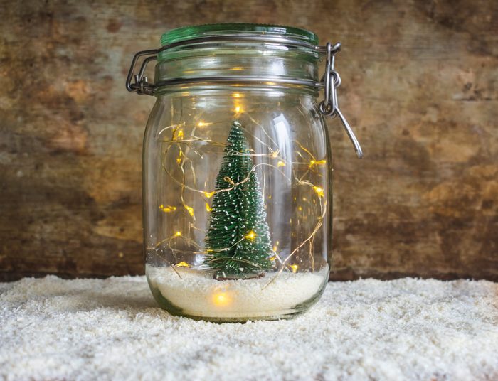 View of a jar with snow and a green Christmas tree decoration and Christmas lights on white snow and a wooden rustic background with copy space. Christmas or winter interior decoration or design 