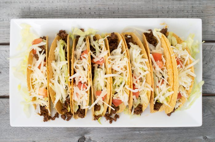 Ground beef tacos with cheese lettuce and tomatoes against wooden background