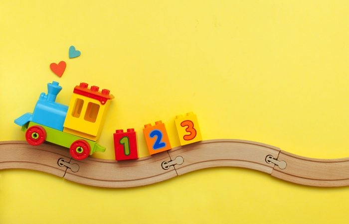 Toys background with copy space. Kids toy train with numbers on toy wooden railway on yellow background with blank space for text. Top view, flat lay.