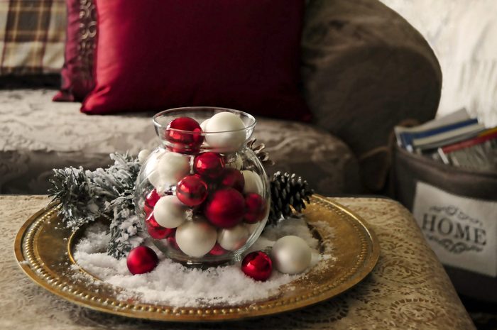 Vintage tray with glass vase filled with red and pearl baubleswith snow and evergreen centerpiece on coffee table by chair with magazine holder saying "home" on the front holding christmas magazine