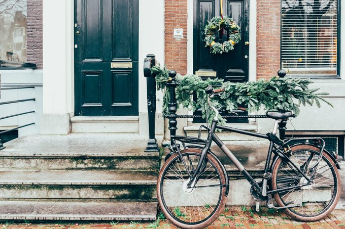 Cozy city picture, a bicycle parked at the entrance to the house decorated with Christmas tree branches.