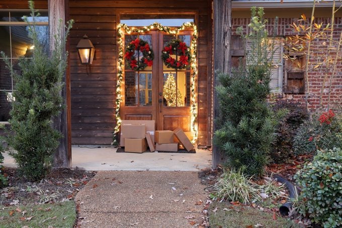 Boxes and packages next to front door during holiday christmas season, with Christmas lights and wreaths