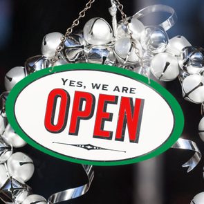 Festive Christmas decorations and open sign with jingle bell wreath hanging in shop store window door during holiday shopping season