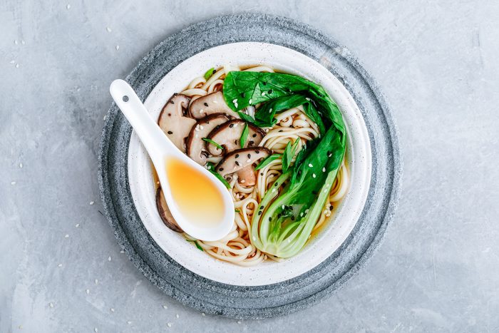 Asian Vegetarian Udon or Ramen noodles soup in bowl with Shiitake mushrooms and Bok Choy on grey stone background