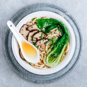 Asian Vegetarian Udon or Ramen noodles soup in bowl with Shiitake mushrooms and Bok Choy on grey stone background