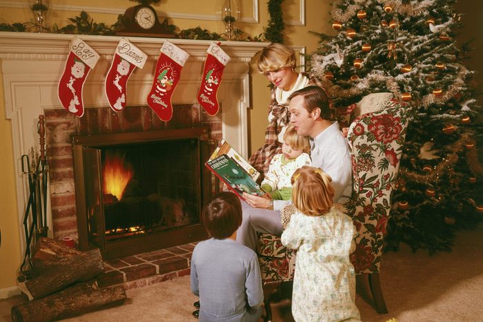 family sitting near the fireplace and christmas tree reading a christmas book