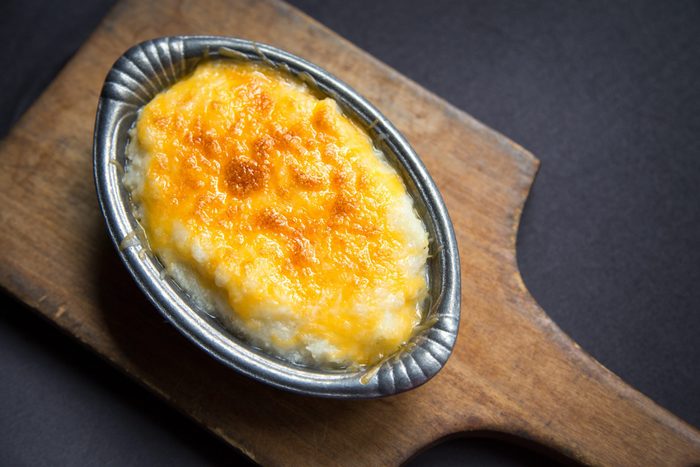 Serving of freshly baked cheese grits in small pewter casserole dish on cutting board.