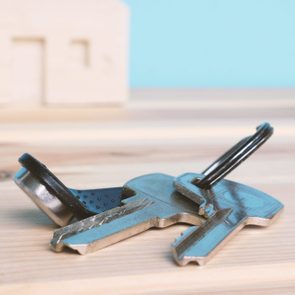 The keys to the apartment with the chip lie on the table against the background of a small wooden house. Concept - the purchase of real estate, housing, home.