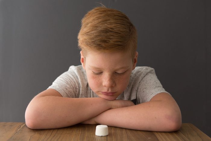 Redhead boy sits at the table opposite a single marshmallow, attempting the marshmallow test