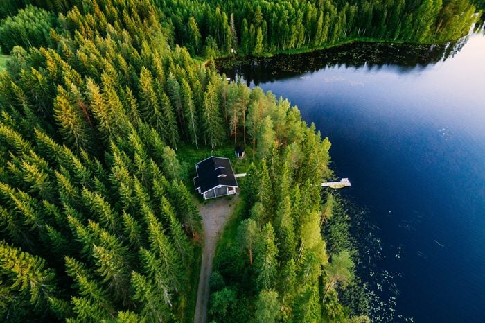 Aerial view of wooden cottage in green pine forest by the blue lake in rural summer Finland