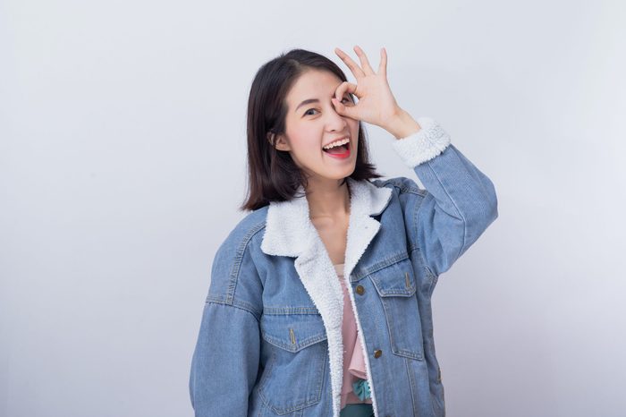 Caucasian smiling woman showing her hand with ok sign, Positive happy young asian girl wearing blue casual clothes portrait in studio