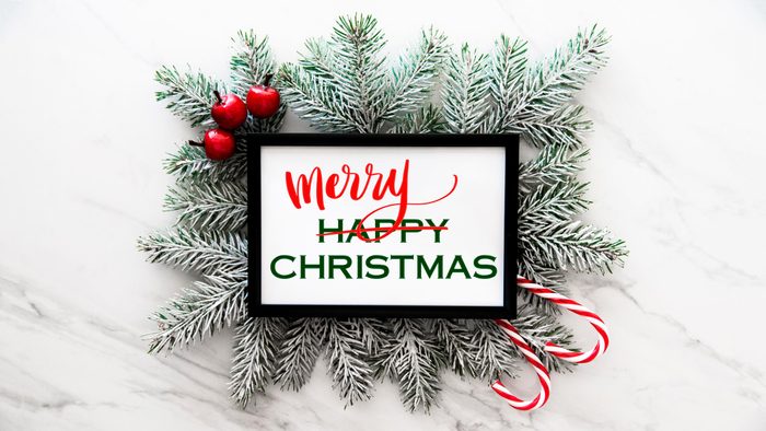 fir tree branches on a marble background with framed white rectangle with text. text reads "happy chirstmas" with "happy" crossed out and "merry" written above