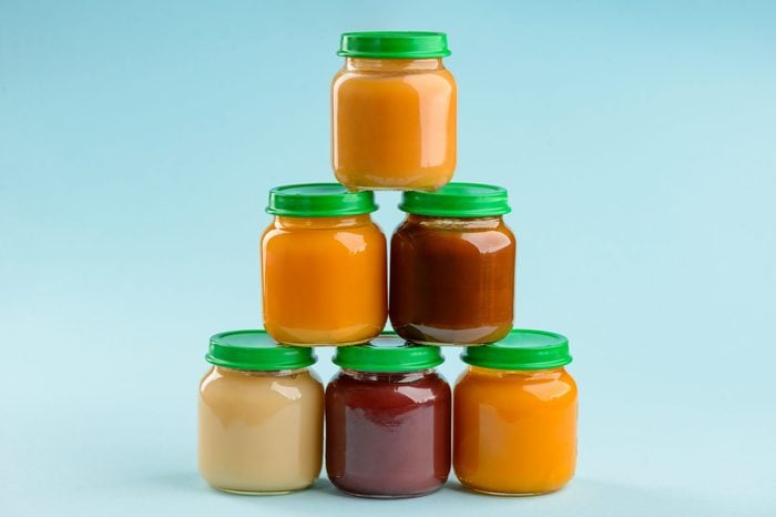 Jars of puree stacked pyramid on blue background. Different tastes of baby food: plum, pumpkin, carrot and banana.