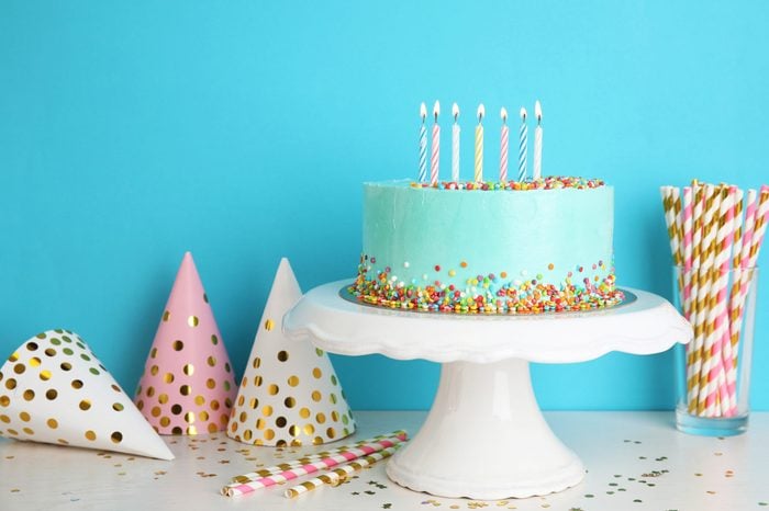 Fresh delicious cake and birthday caps on table against color background. Space for text