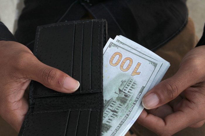 a man pulls cash from his wallet that shows one hundred dollar bill.