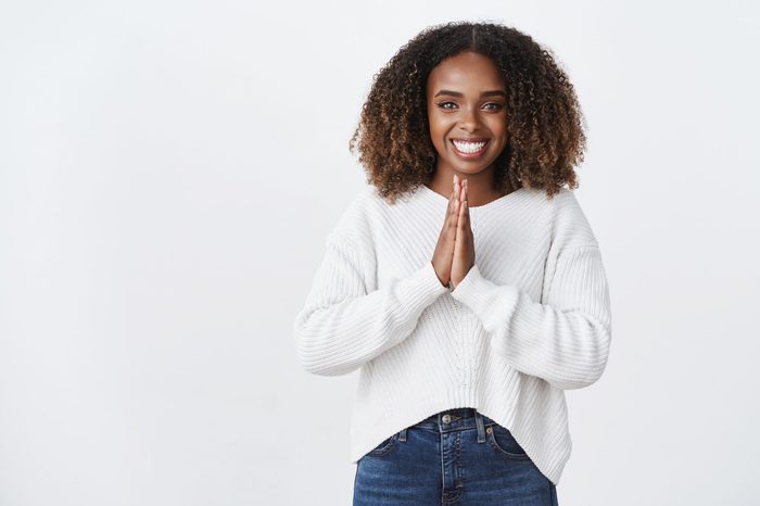 Please do me favor. Charming pleasant friendly-looking african american smiling woman press palms together supplication, pray gesture asking help, grinning thankful lend money white background