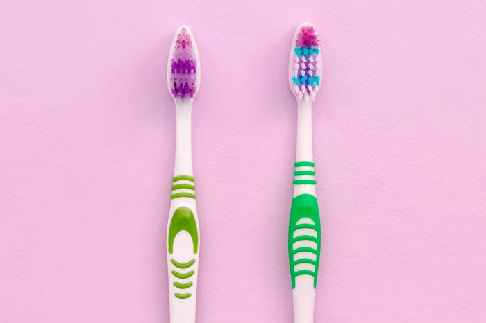 Two toothbrushes lie on a pastel pink background